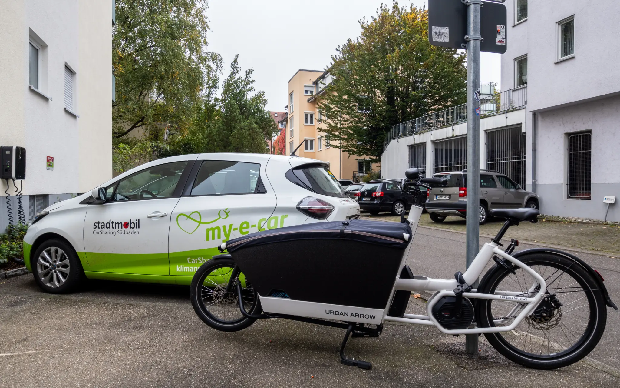 Vélo cargo électrique Urban Arrow stationné en ville, à côté d'une voiture en autopartage