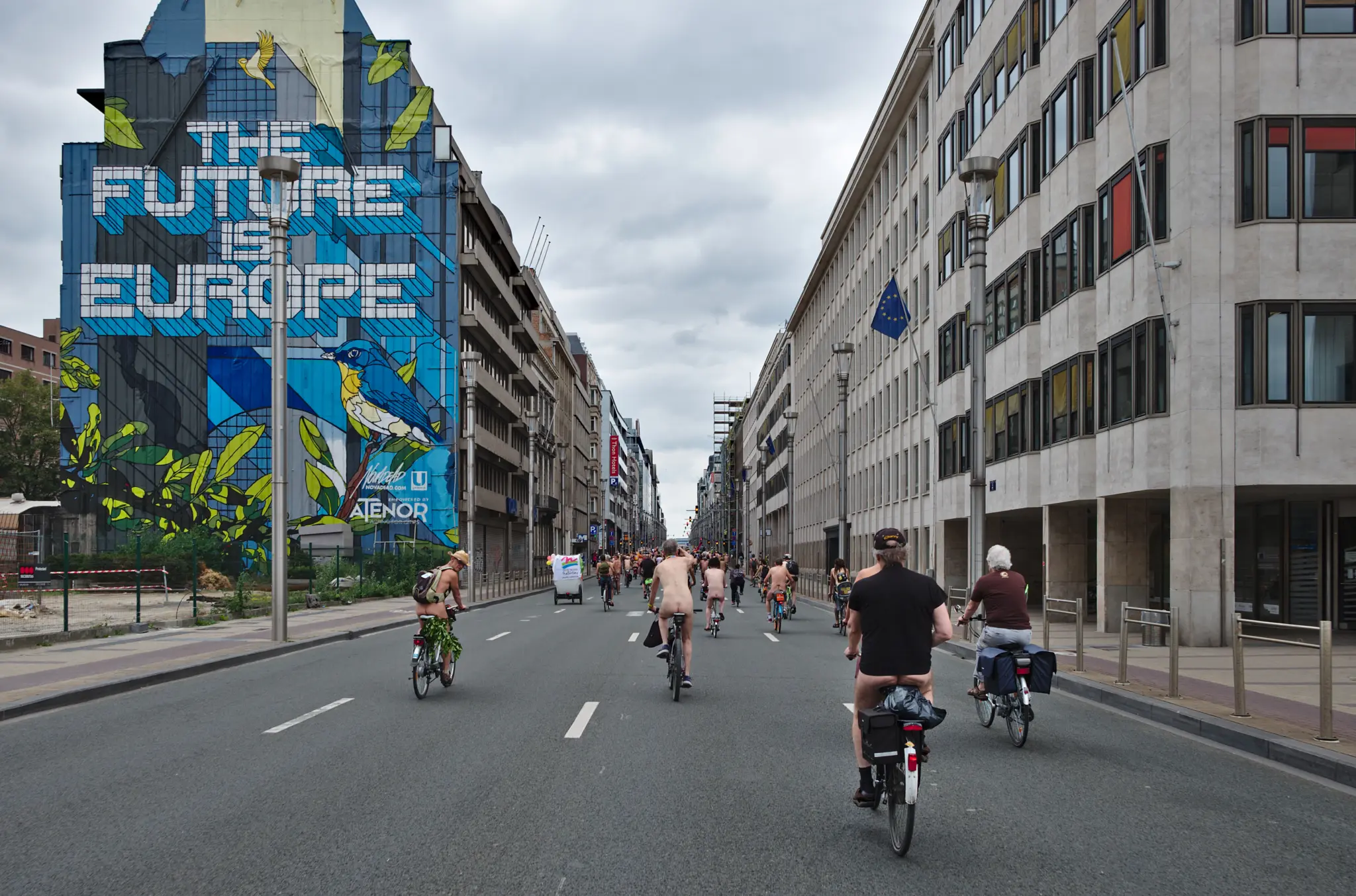 Cyclistes de dos sur une avenue bruxelloise lors de la World Naked Bike Ride, devant une fresque The Future is Europe