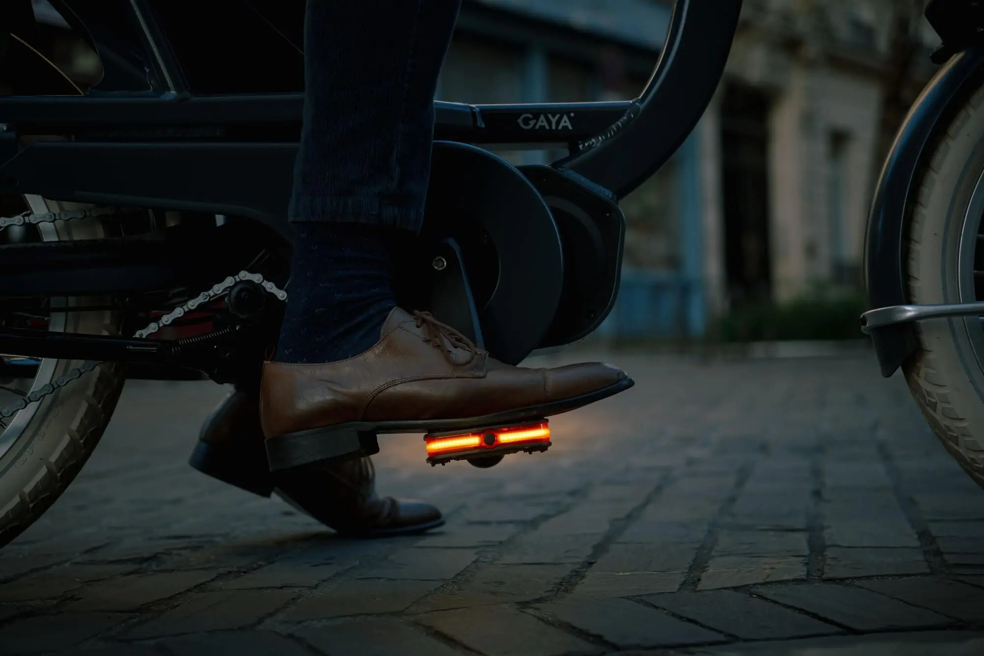 Chaussure de ville posée sur une pédale Look Geo City Vision dont la bande LED orange est allumée, de nuit