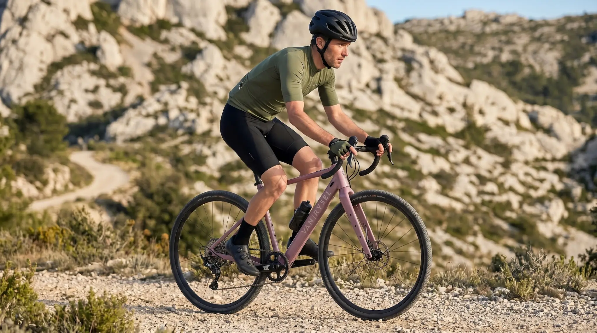 Cycliste roulant sur le gravel électrique Van Rysel E-GRVL AF HD X30 rose taupe dans un paysage rocailleux