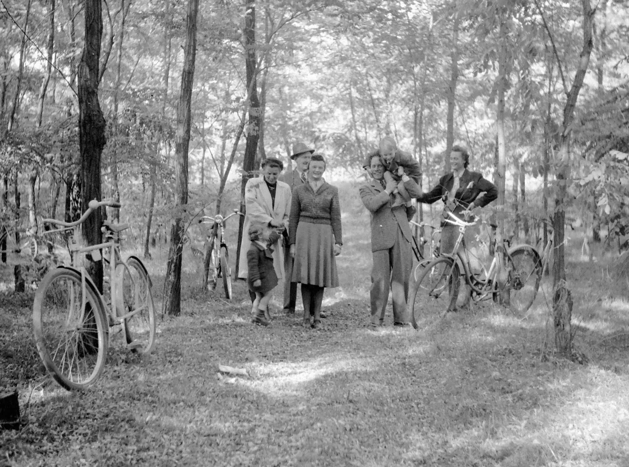Groupe de promeneurs en tenue des années 1930, leurs bicyclettes appuyées aux arbres, sur un chemin forestier