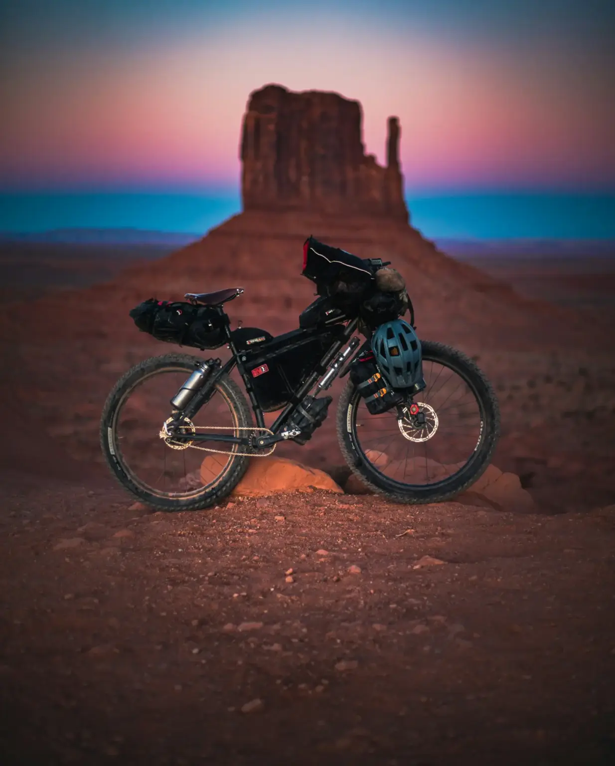Vélo de bikepacking chargé de sacoches, posé sur la terre rouge devant une butte de Monument Valley au crépuscule