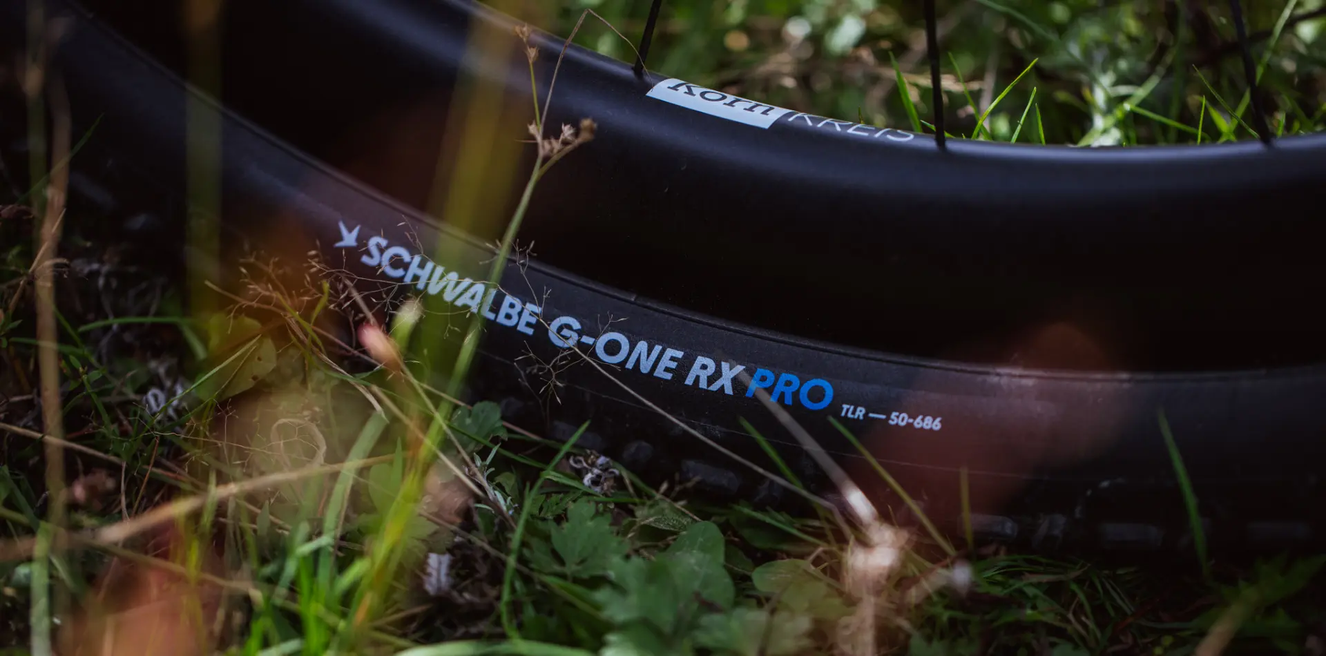 Flanc d'un pneu posé dans l'herbe, portant le marquage SCHWALBE G-ONE RX PRO TLR 50-686