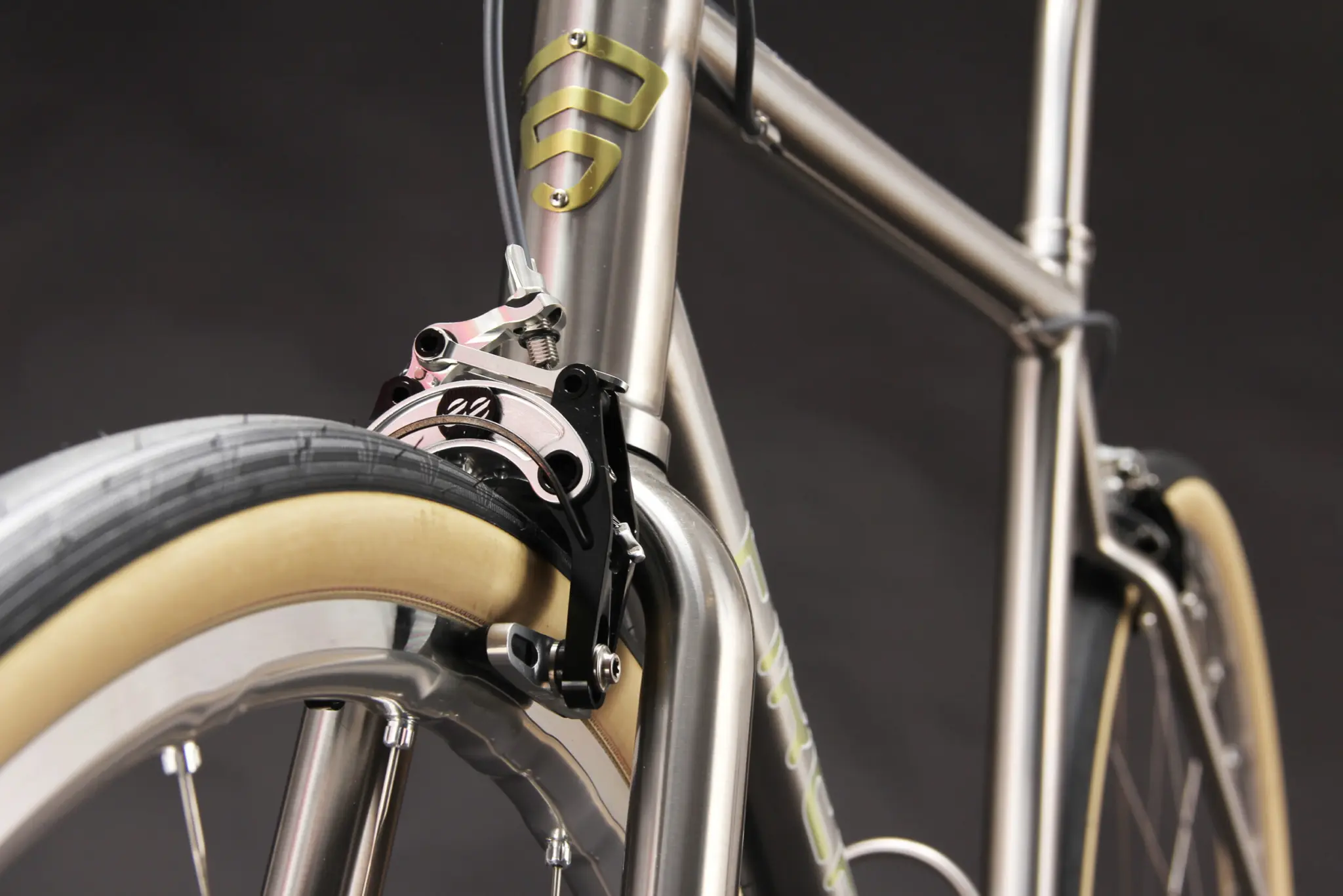 Étrier de frein sur jante avant noir et argent monté sur la couronne de fourche titane du Firefly All Road Rim Brake, pneu large à flanc beige