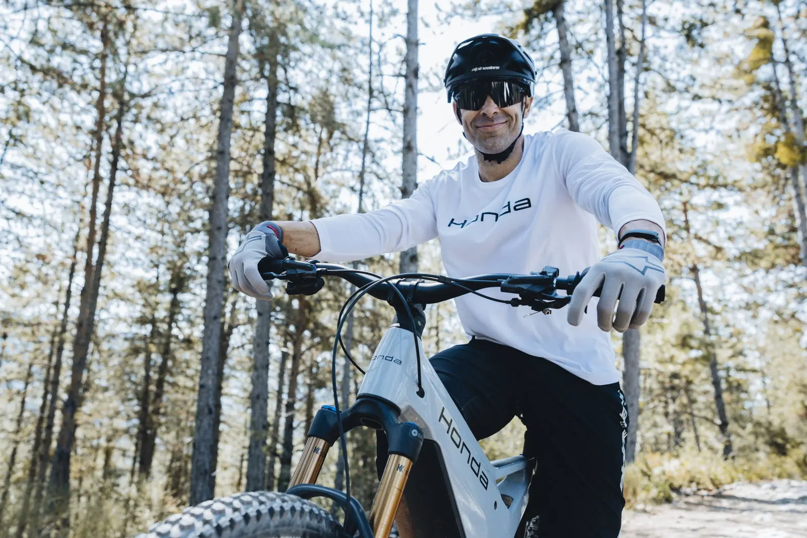 Toni Bou, in a white Honda helmet and jersey, sitting on the Honda e-MTB Prototype in a forest