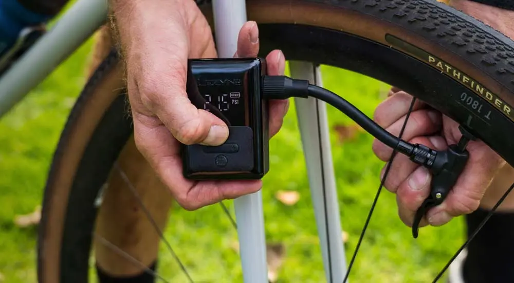 Un cycliste tient l'E-Drive dans la main, flexible raccordé à la valve d'une roue de gravel