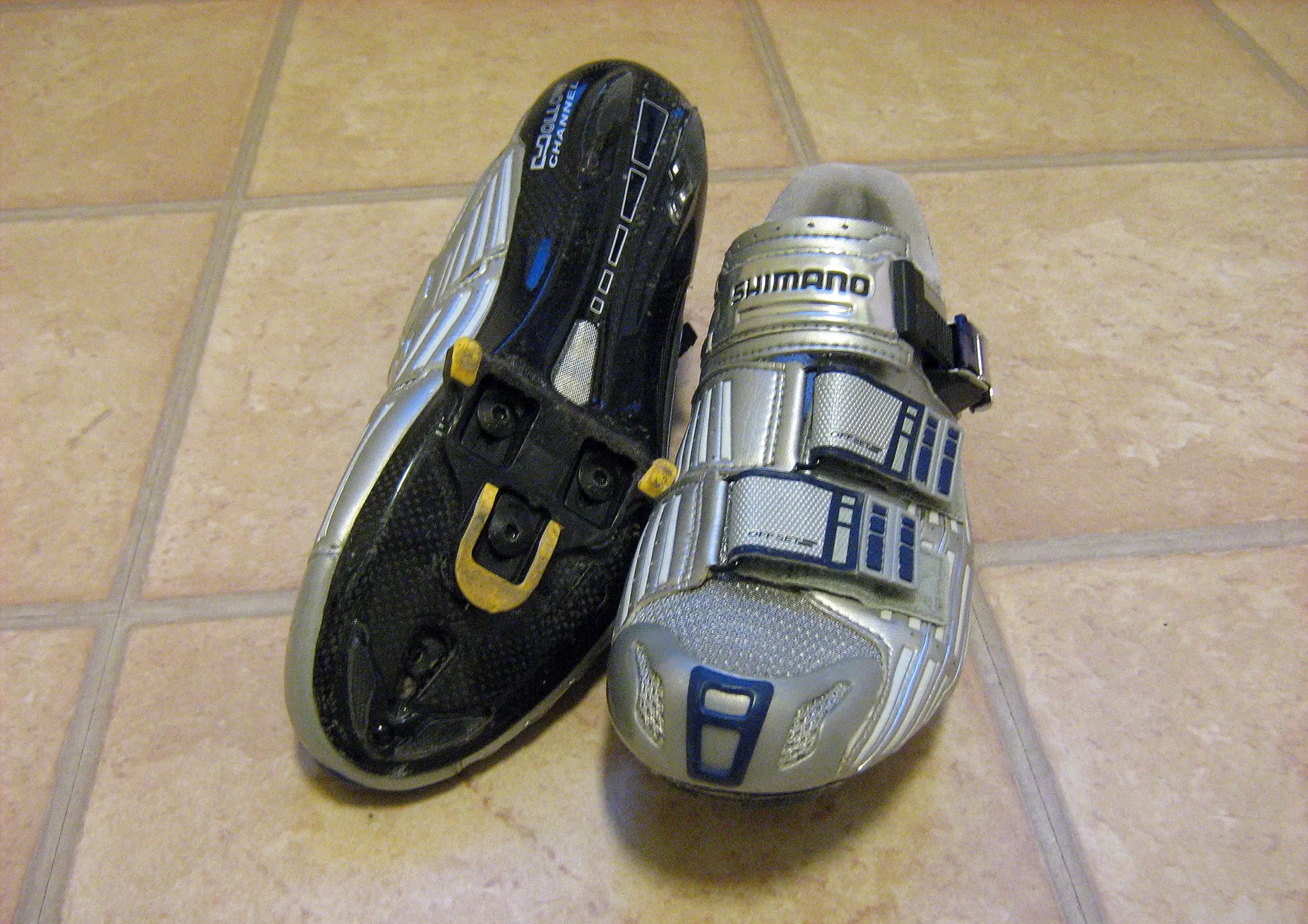 Paire de chaussures de vélo route Shimano, l'une retournée pour montrer la cale SPD-SL jaune fixée sous la semelle