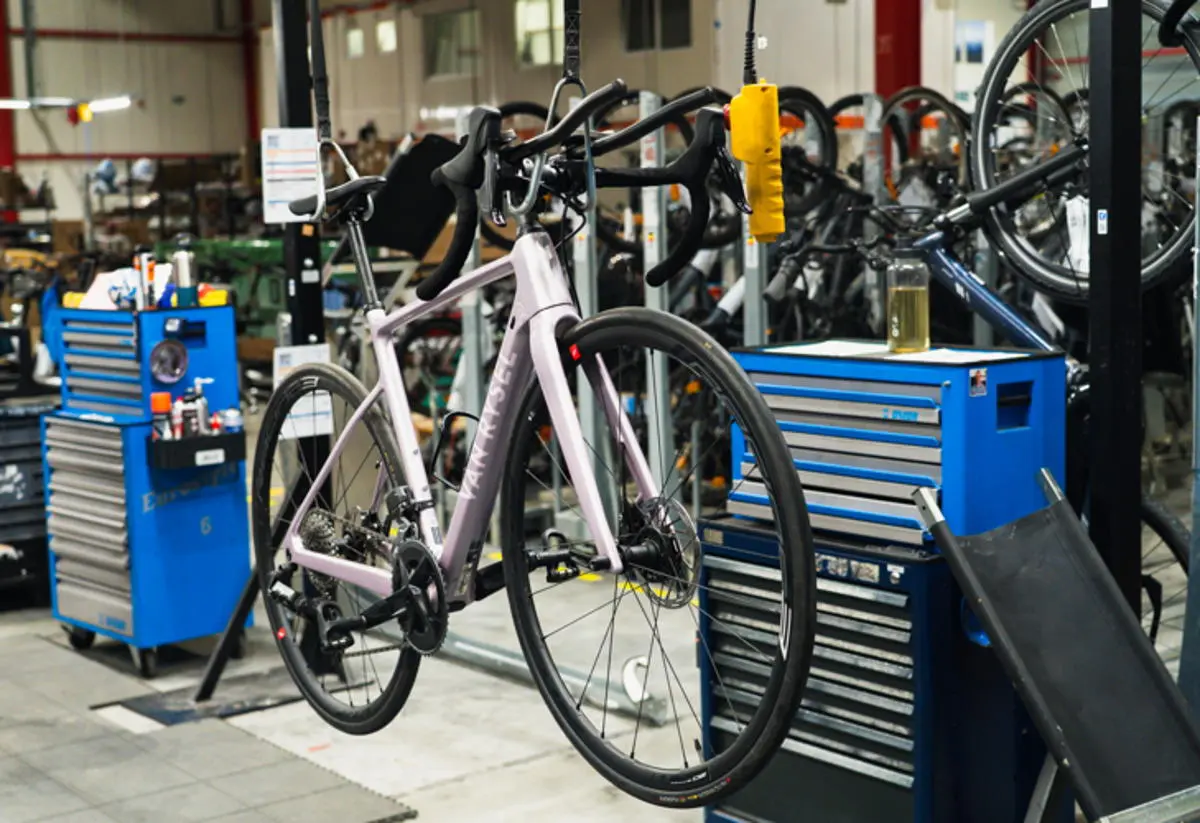 Vélo de route rose clair du programme re-lease, monté sur un pied d'atelier, entouré de servantes à outils