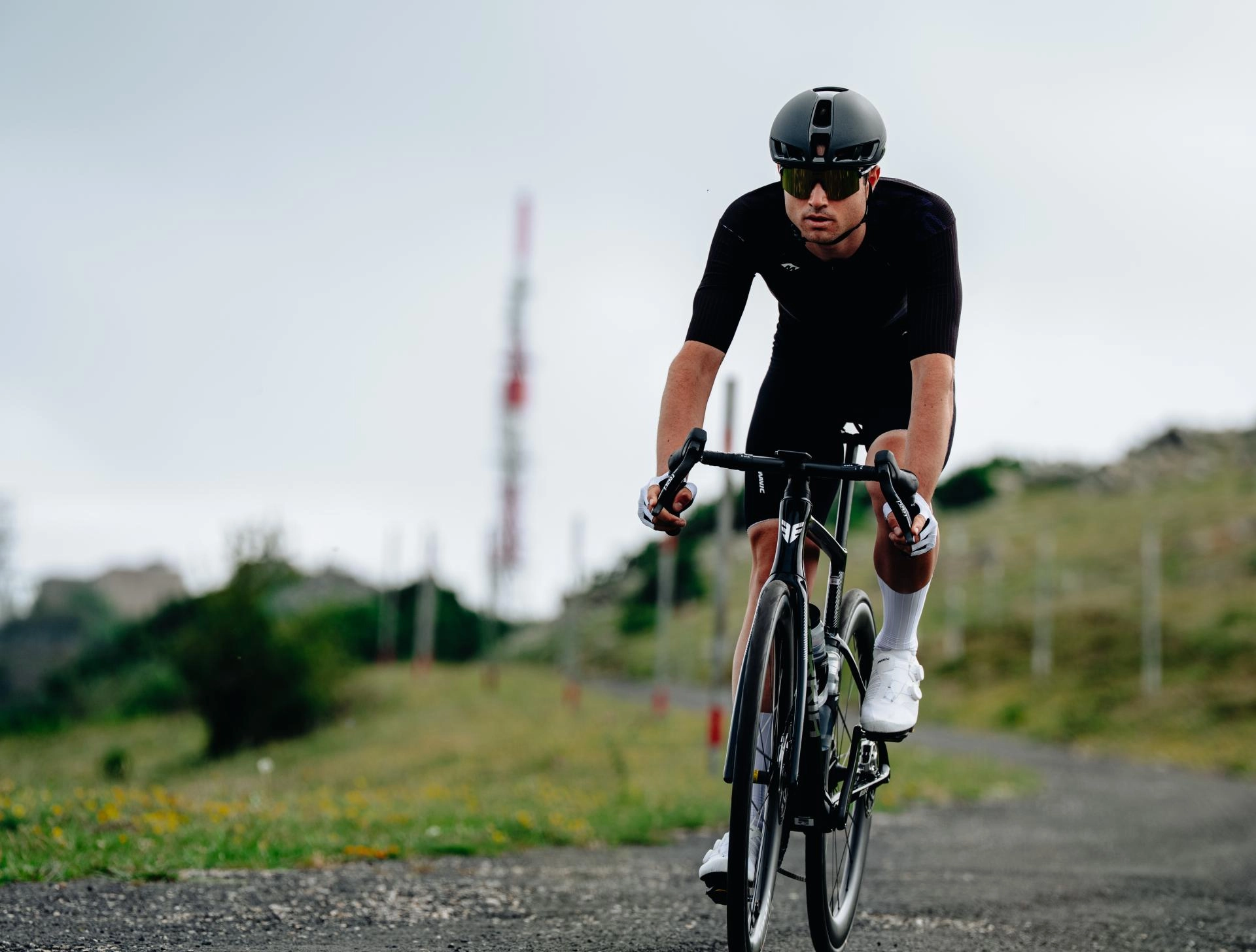 Cycliste en tenue noire sur une route de montagne, coiffé d'un casque Mavic gris foncé