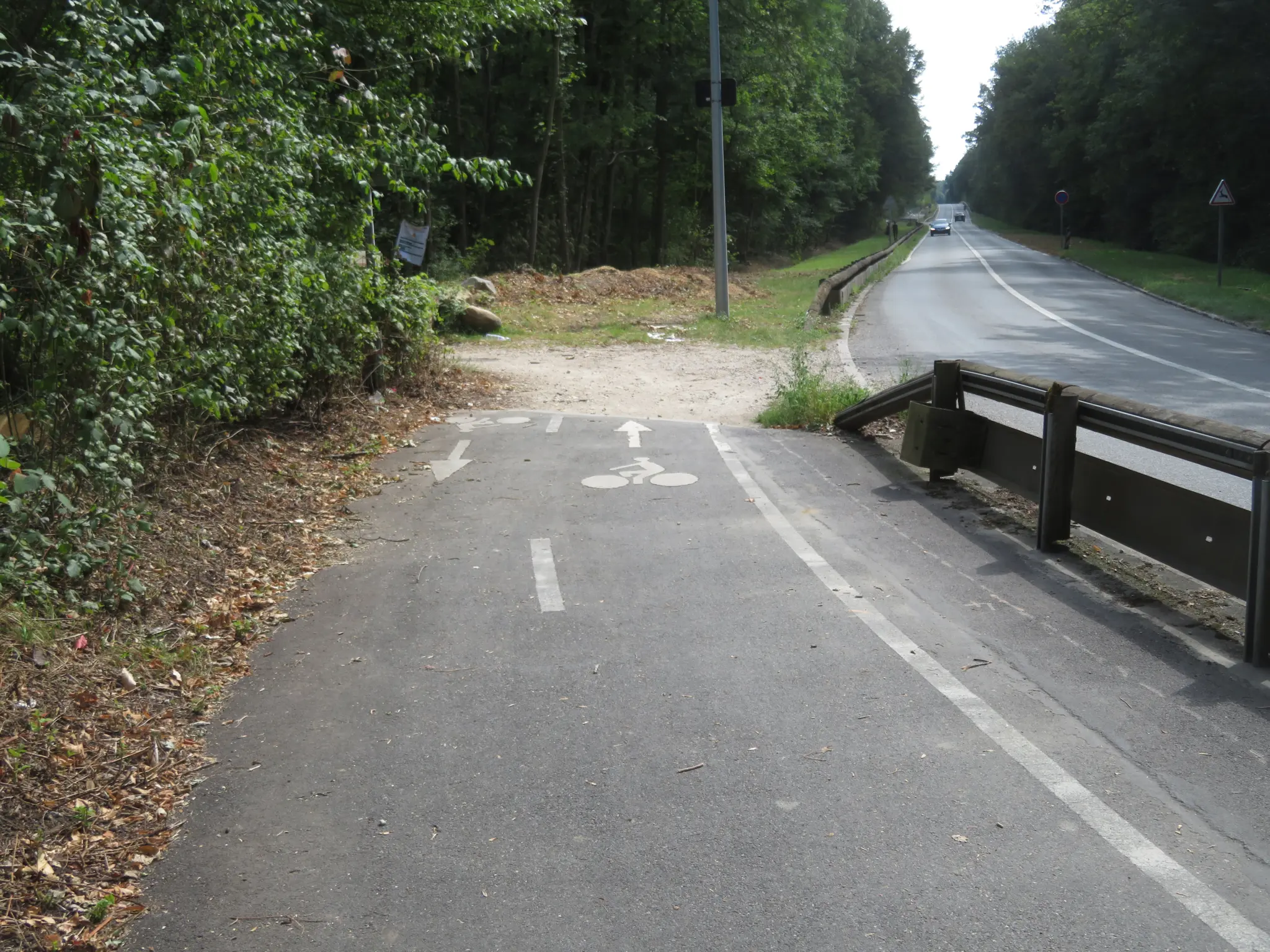 A break on a cycle route, of the kind the Vélo Île-de-France plan targets: a surfaced cycle path stops abruptly on an earth bank, beside a departmental road protected by a crash barrier