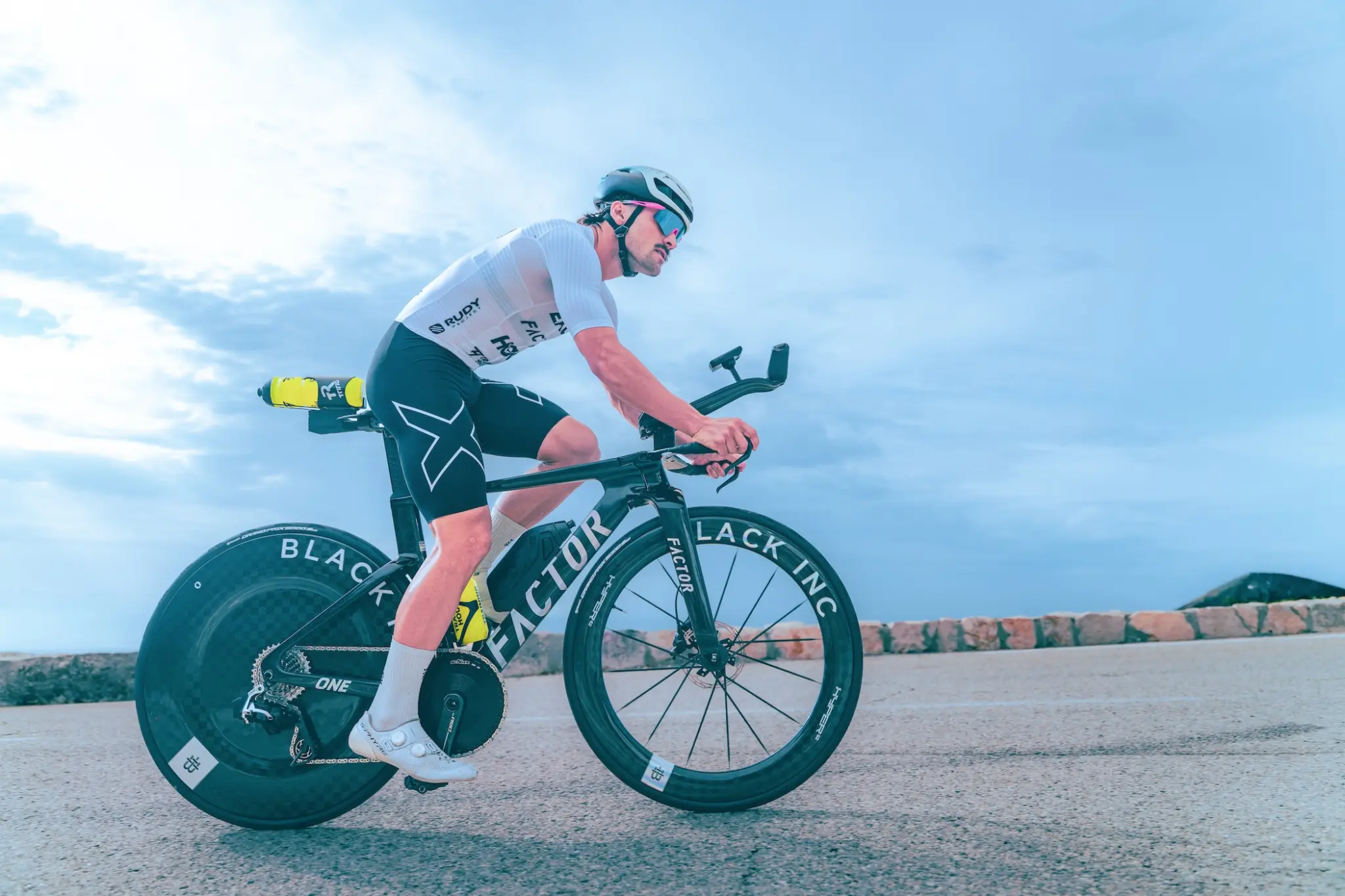 Un triathlète en position de chrono sur le Factor ONE SP, roue lenticulaire Black Inc à l'arrière, sur une route de corniche