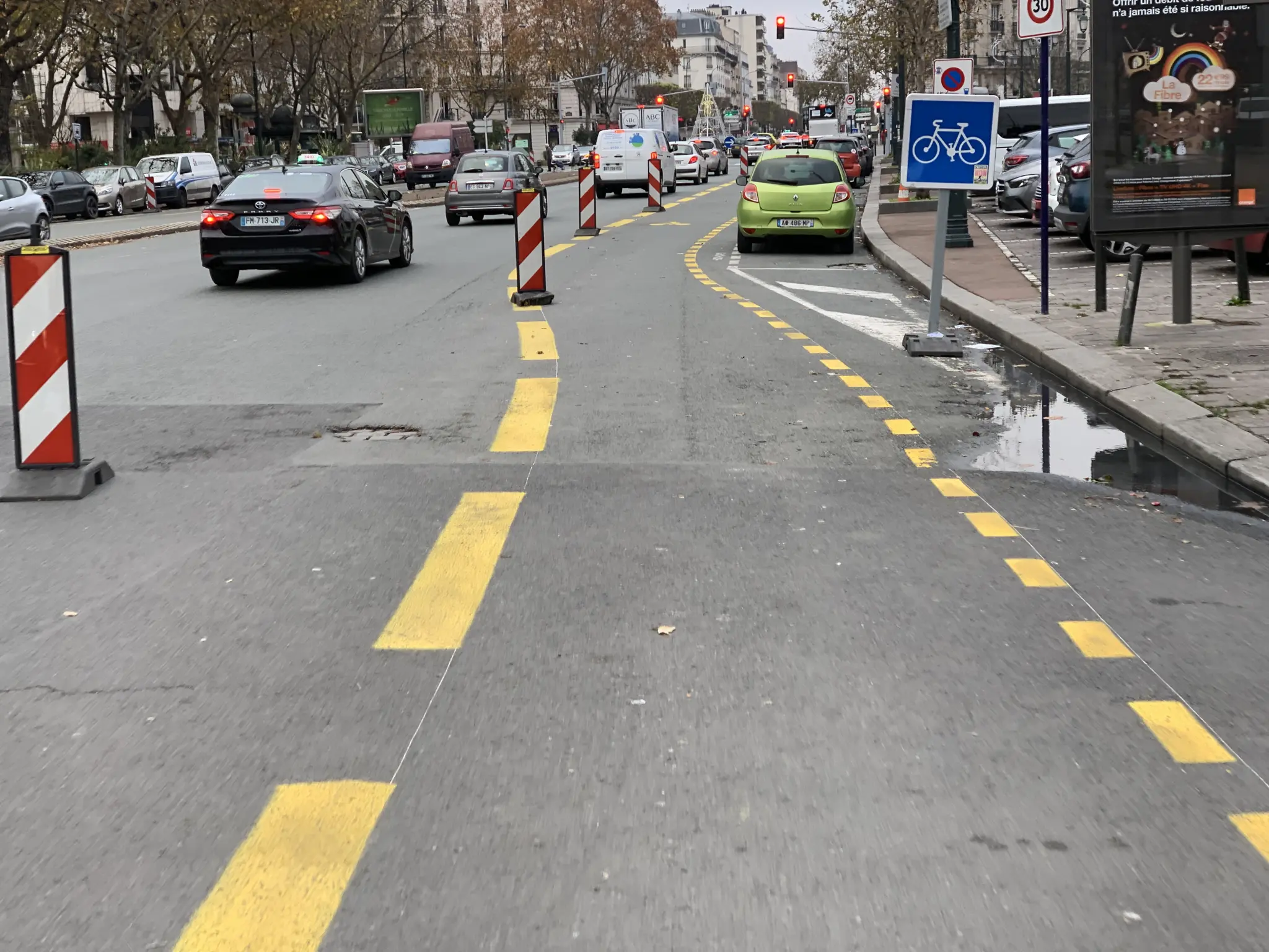 Cycle lane marked out with temporary yellow paint and works beacons along an urban avenue, with a cycle signpost