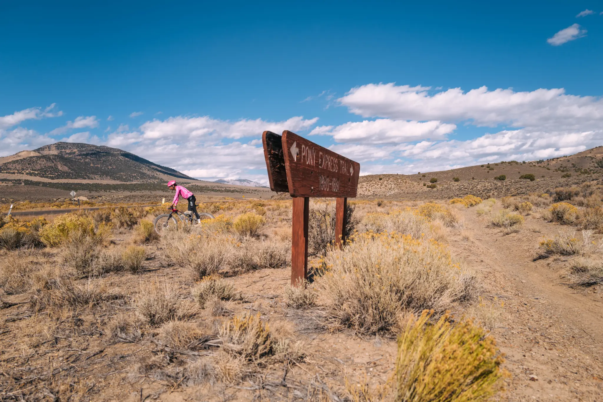 Lachlan Morton à vélo passant près d'un panneau du sentier du Pony Express dans un paysage aride