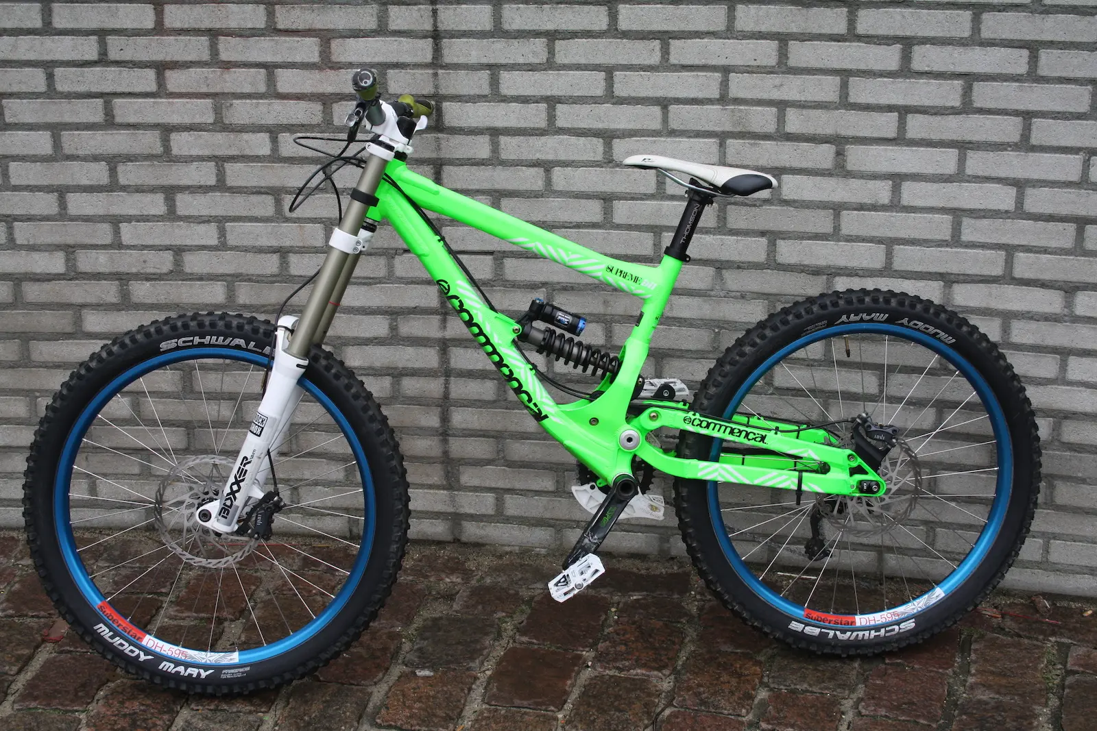 VTT de descente vert avec fourche et amortisseur arrière, devant un mur de briques