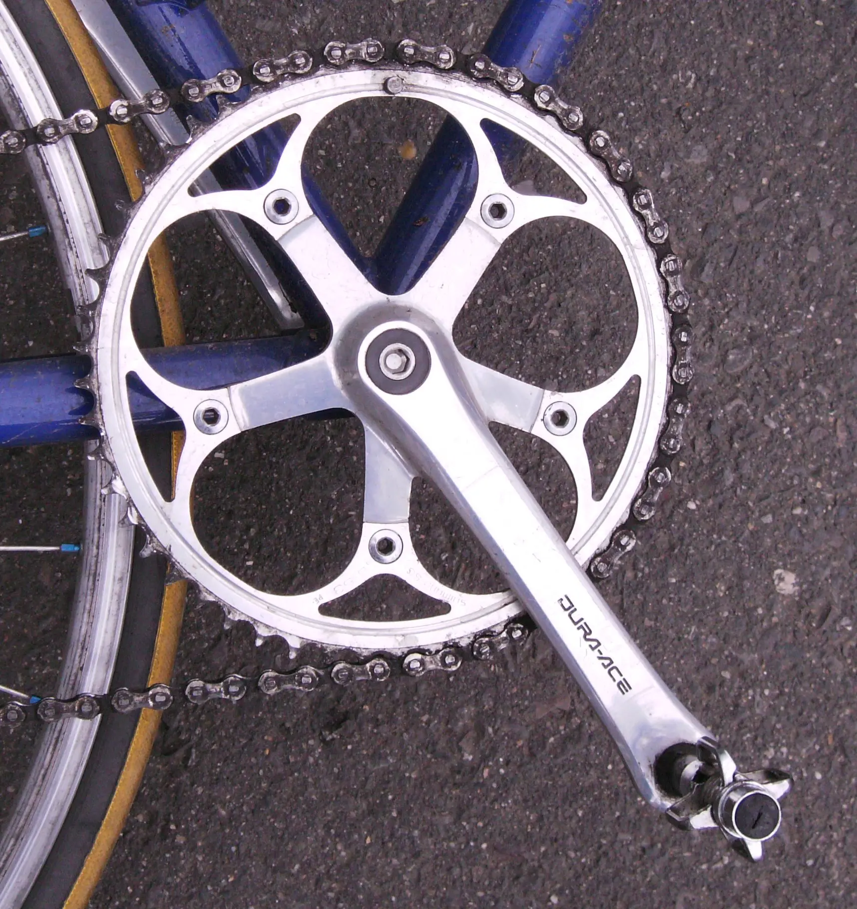 Un ancien pédalier Shimano Dura-Ace argenté monté sur un vélo à cadre bleu