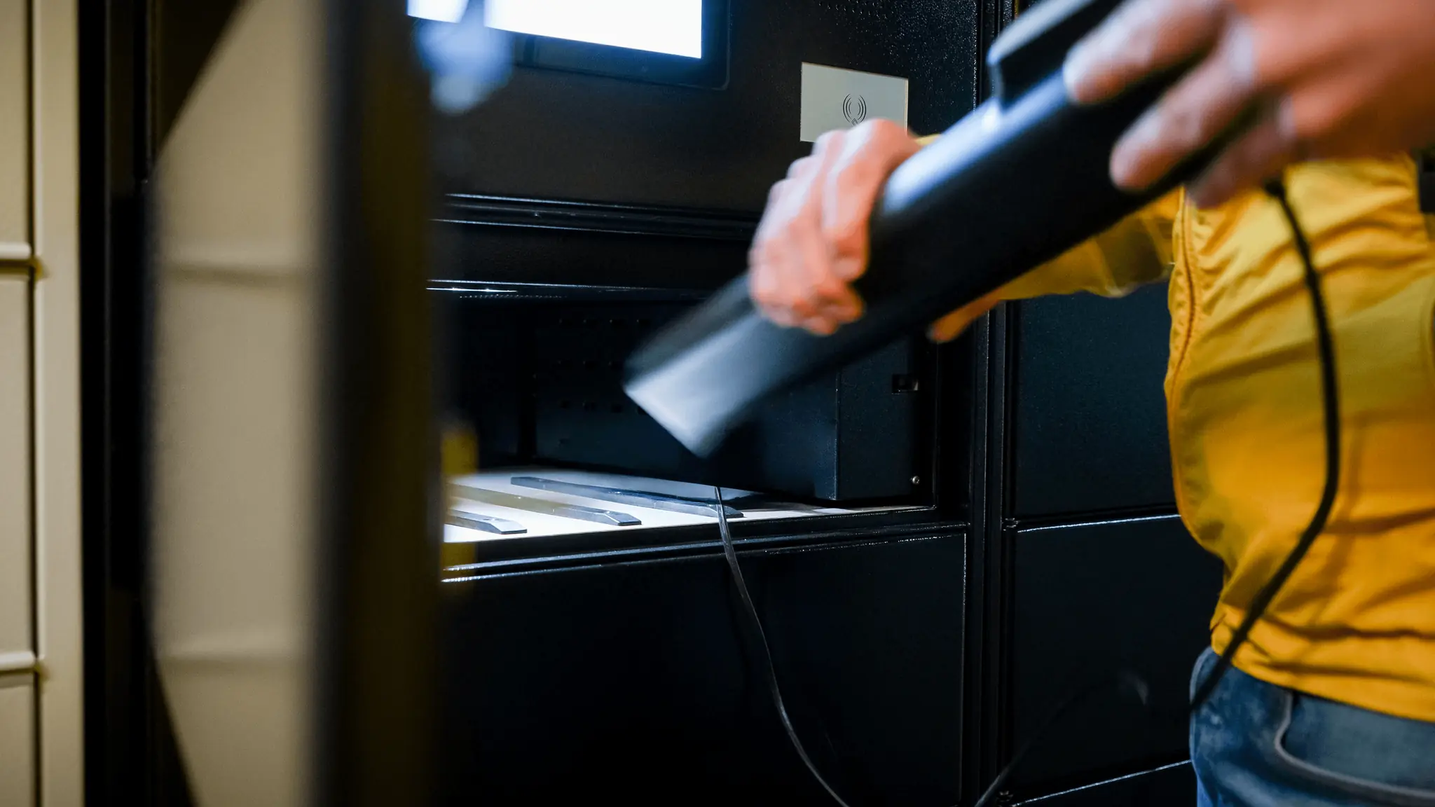 Compartiment ouvert d'un casier de recharge PowerShelter, une personne manipule un chargeur de batterie de VAE