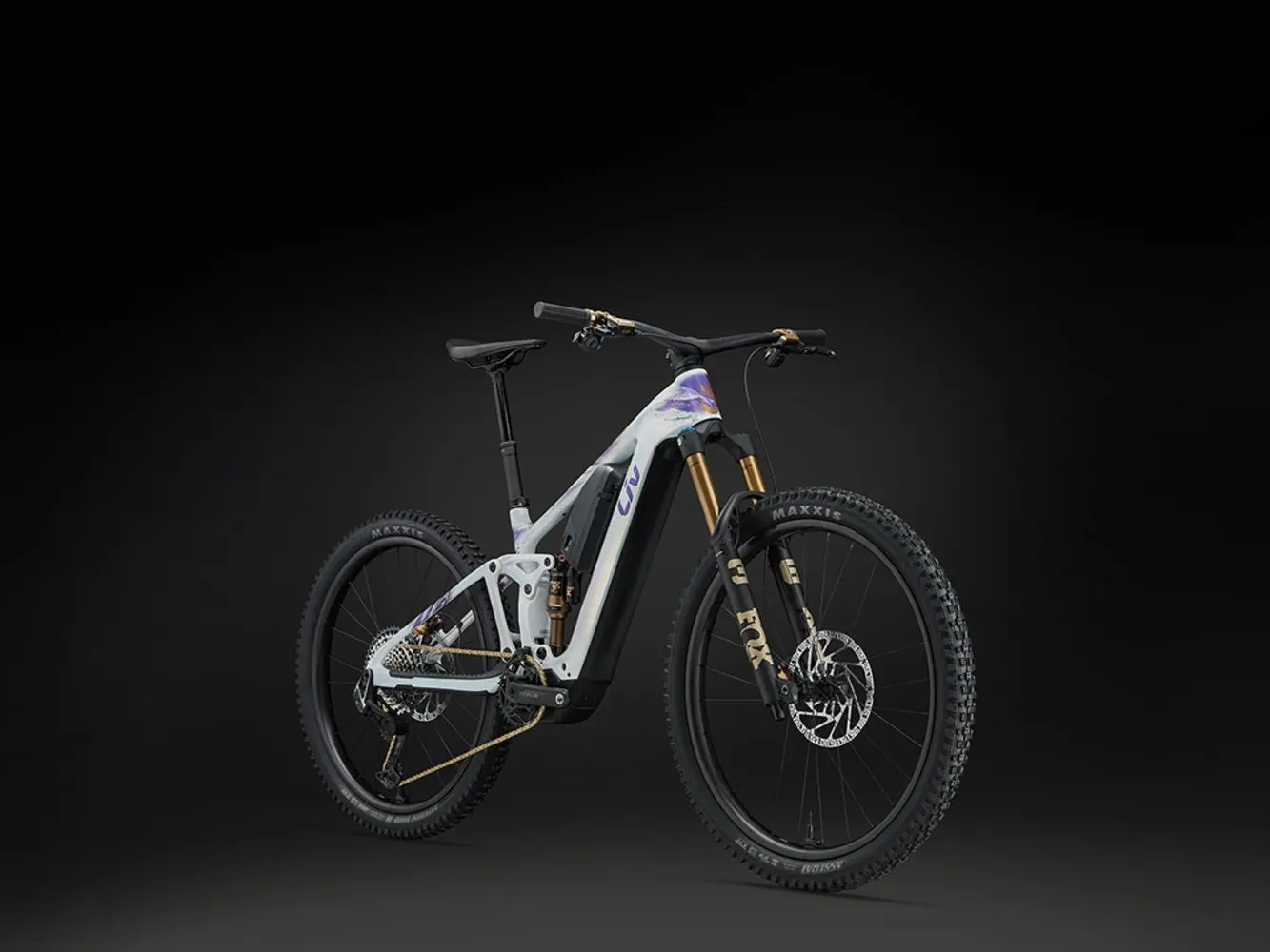 Le VTT électrique Liv Intrigue Advanced E+ vu de trois quarts sur fond noir, cadre blanc irisé et fourche Fox
