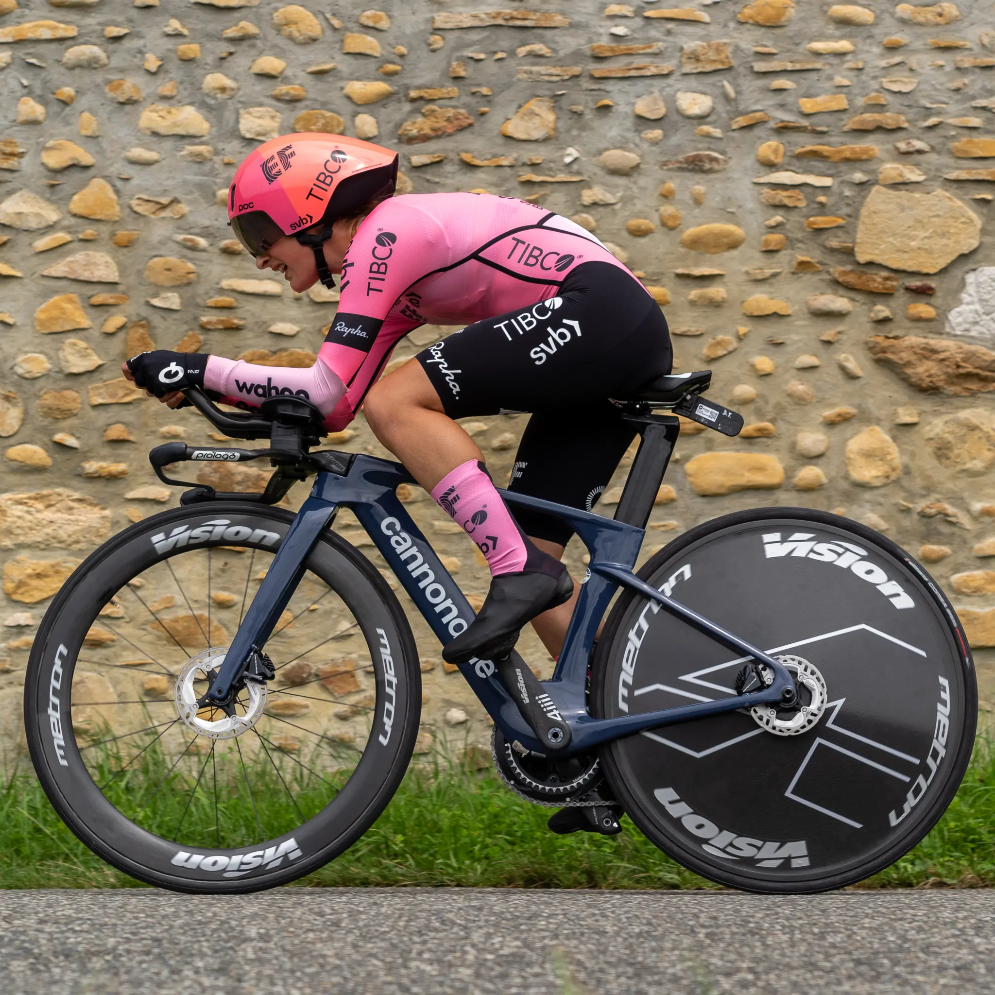 Time trial at the 2023 Tour de France Femmes: a rider in a pink skinsuit on a time trial bike with a disc wheel, in front of a stone wall