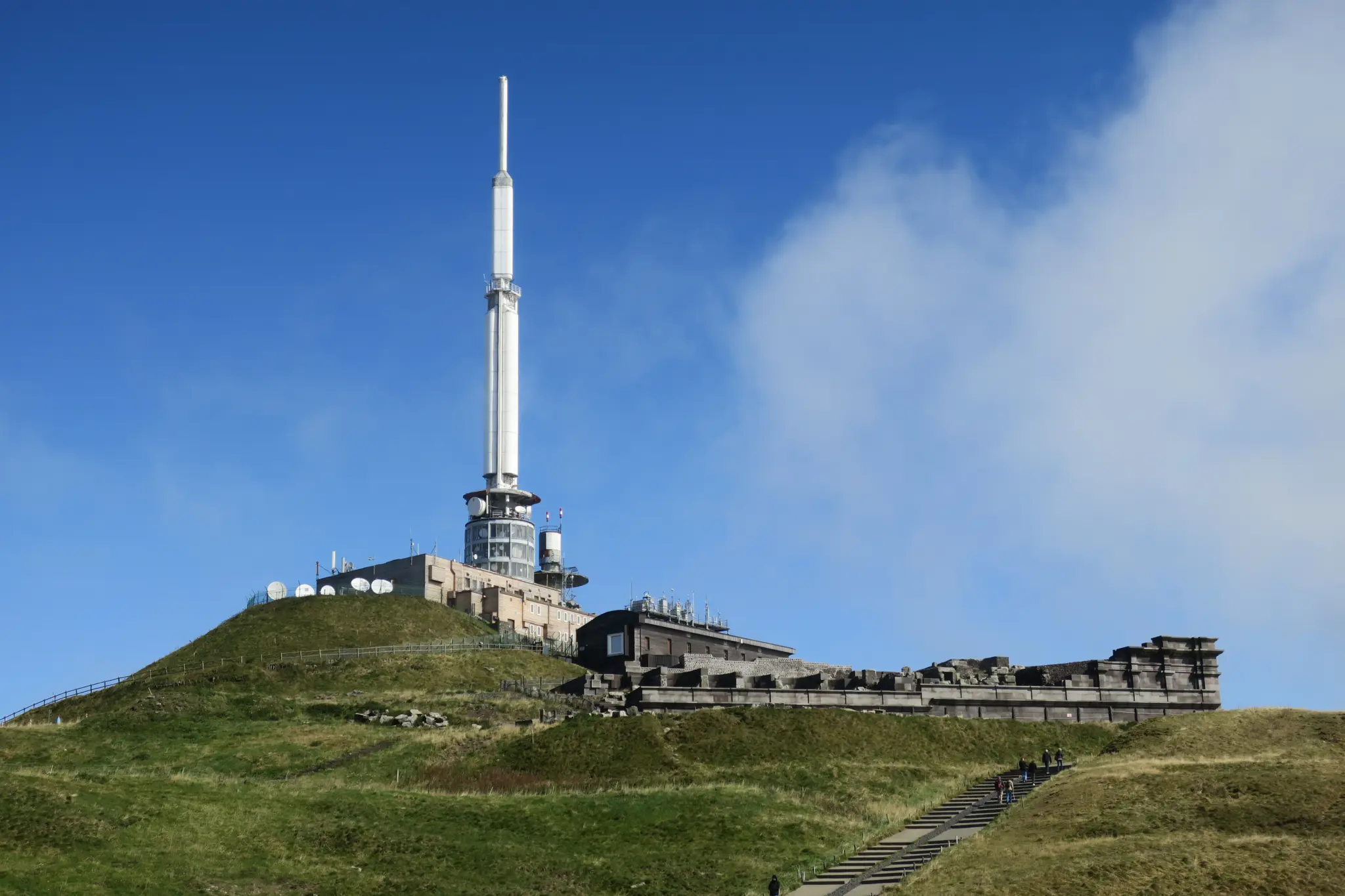 The grassy summit of the Puy de Dôme, with its antenna and summit buildings under a blue sky