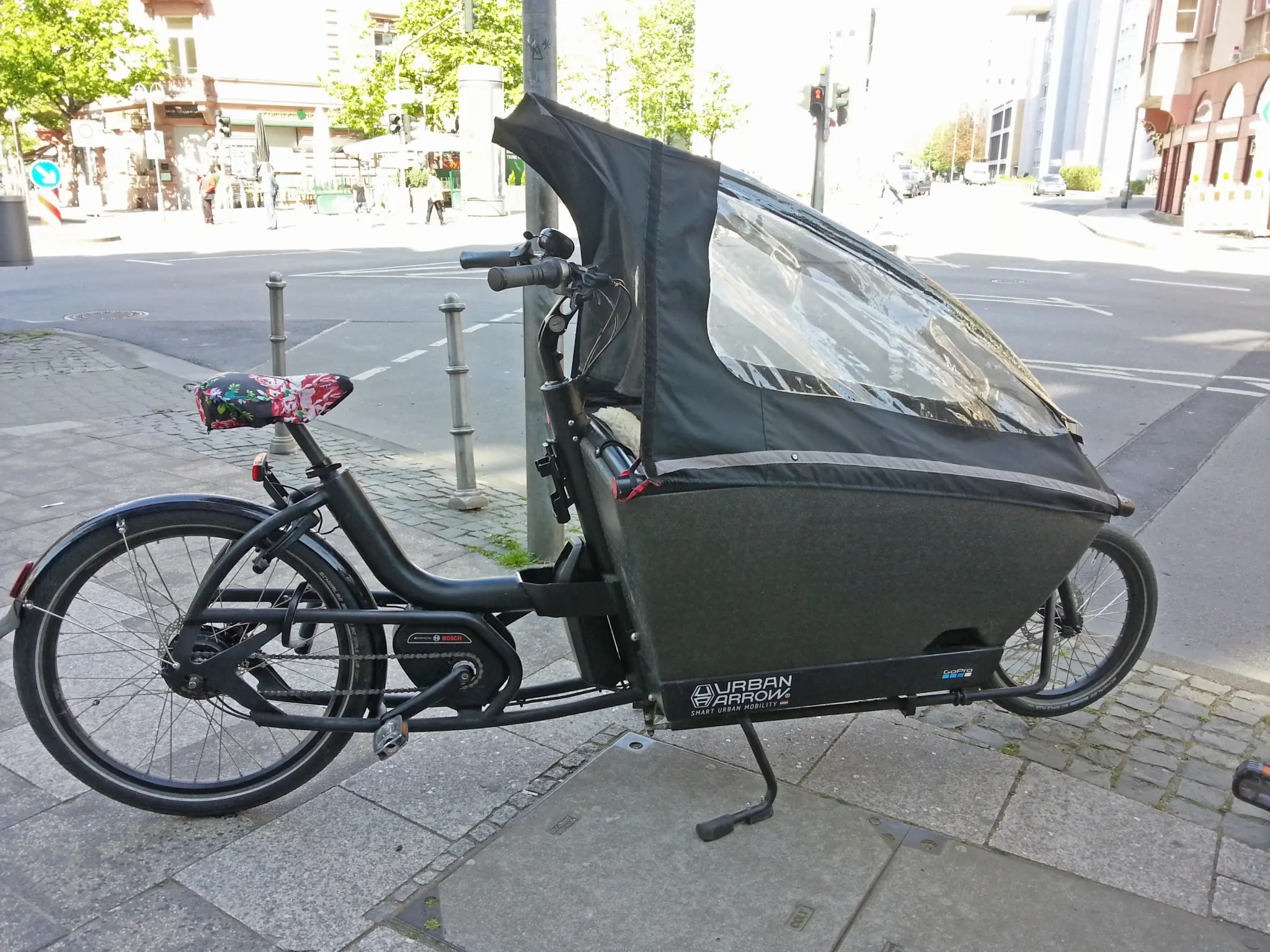 Urban Arrow electric box bike with cargo box and rain cover, parked on a pavement in Frankfurt in 2019