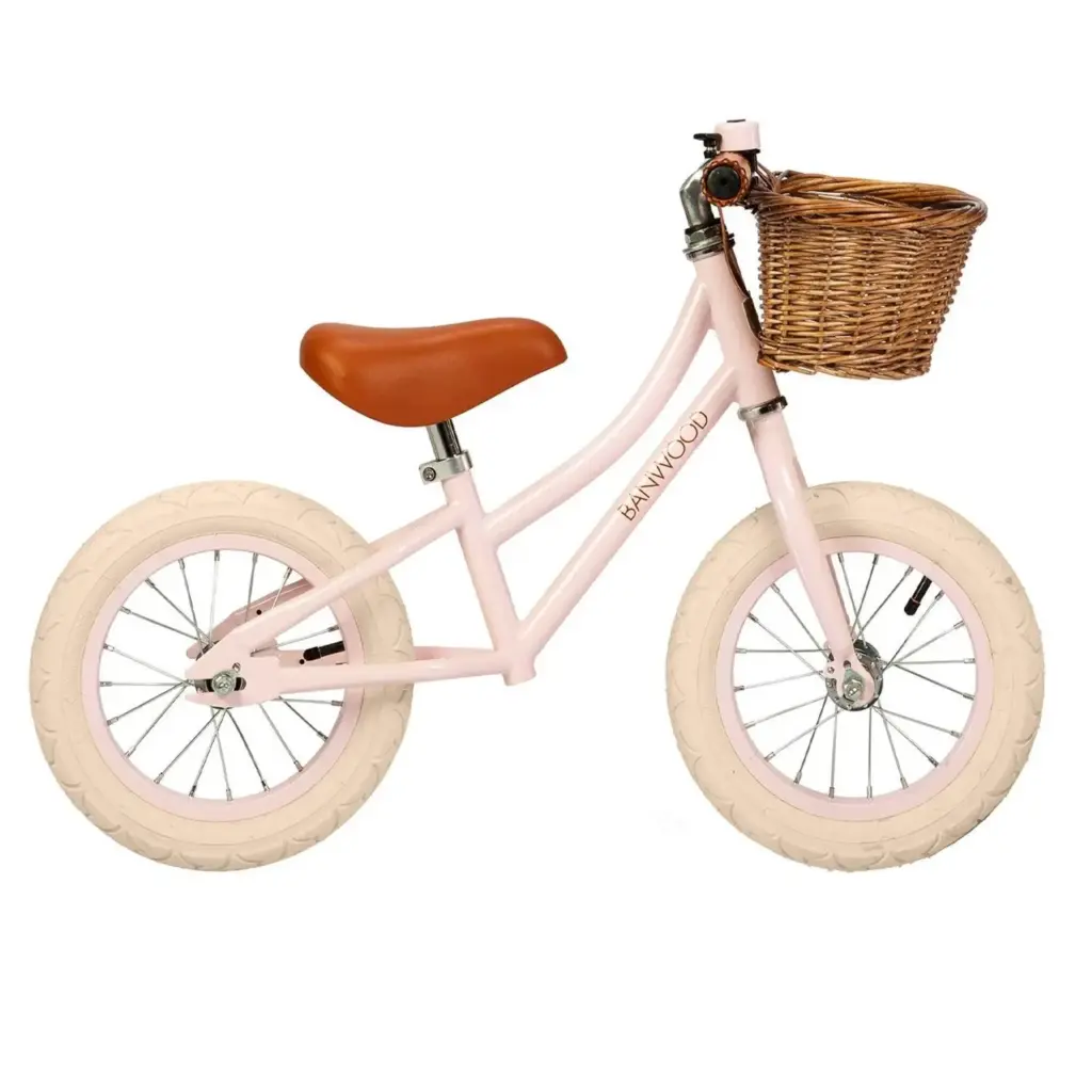 La draisienne Banwood First Go rose pâle, avec sa selle marron et un panier en osier