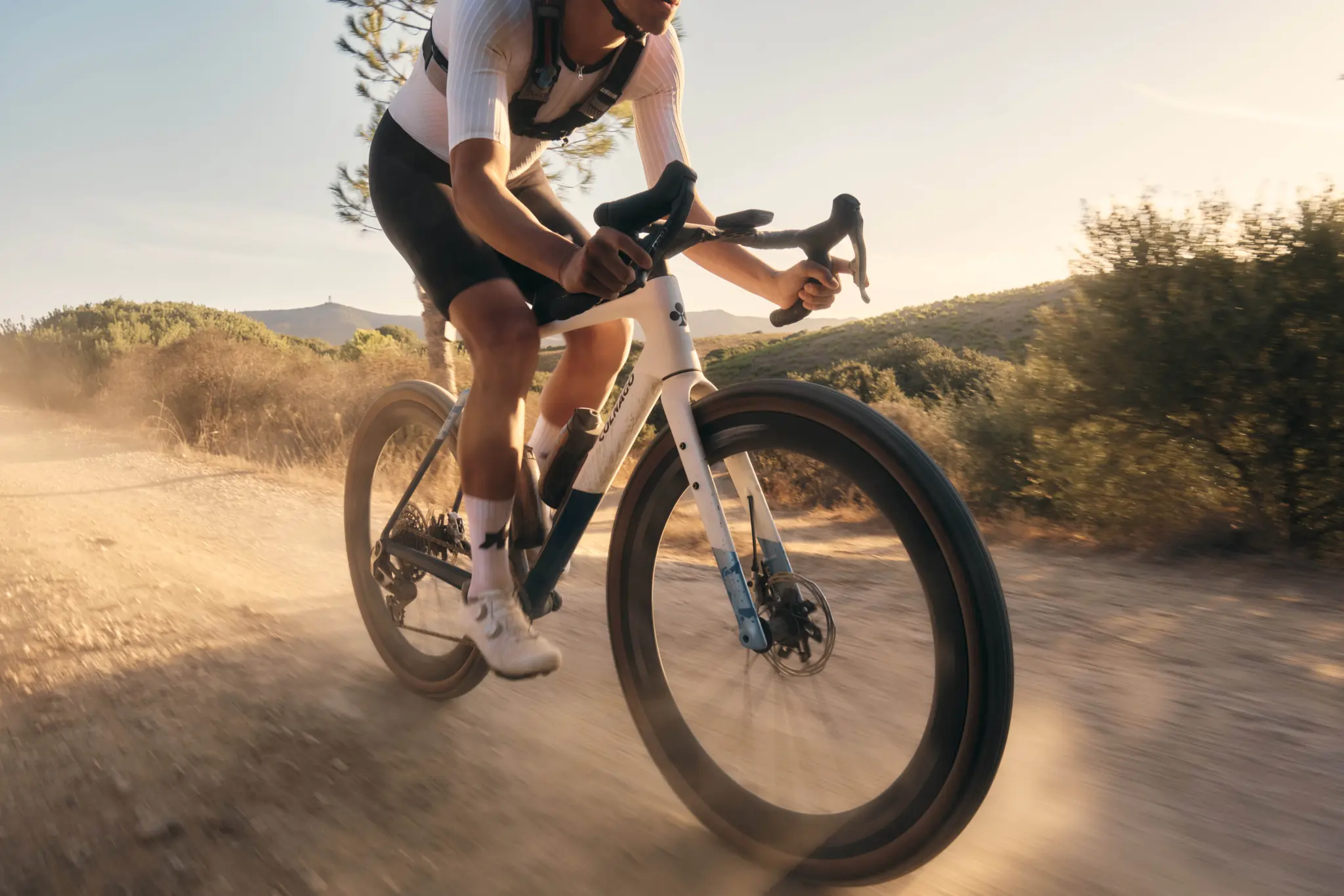 A rider kicks up dust on a dirt track aboard the white and blue Colnago G5-X gravel bike