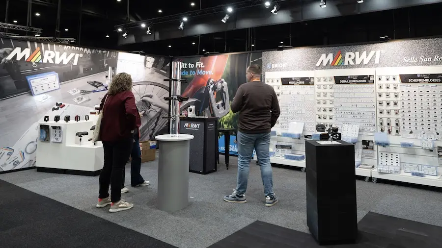 Exhibitor stand for bicycle parts with printed walls and display racks, two visitors